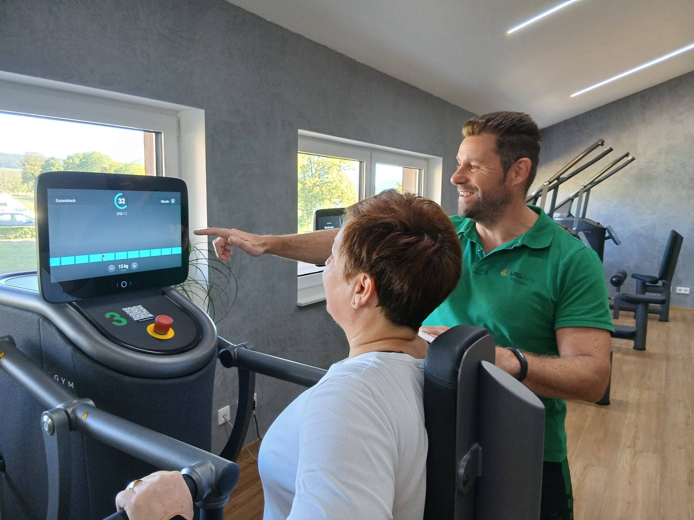 Trainingsleiter Michael erklärt einem Mitglied die Anzeige an einem EGYM-Gerät